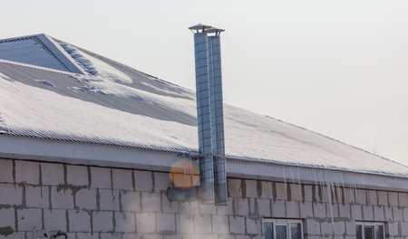 A chimney on a roof with snow on it. The chimney is on the side of a buildingの写真素材