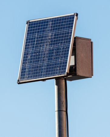 A solar panel is on a pole. The solar panel is black and silver. The pole is metalの写真素材