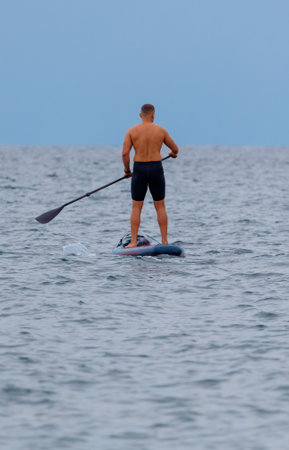 A man is standing on a surfboard in the ocean. He is wearing shorts and a shirt