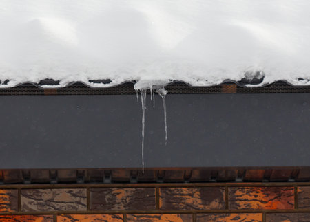 A roof has icicles dripping from it. The roof is covered in snowの写真素材