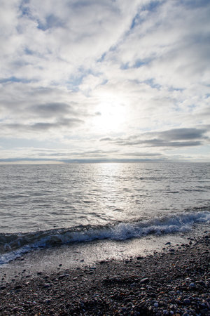 The sky is cloudy and the sun is shining on the ocean. The water is calm and the beach is rockyの写真素材