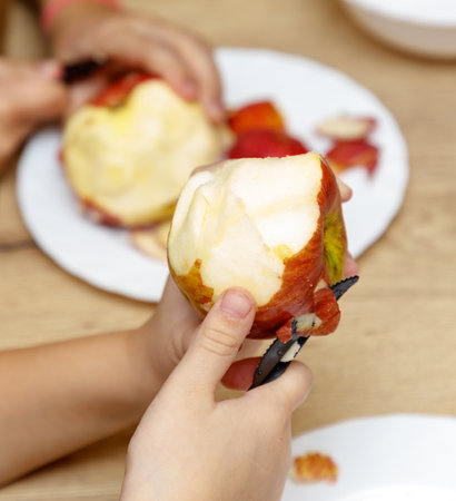 A person is holding a knife and cutting an apple. The apple is on a plate. There are other people in the backgroundの写真素材