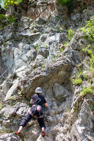 Man is climbing a rock wall. He is wearing a black shirt and black pants. He is wearing a helmet and...