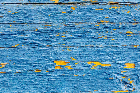 A blue and yellow wooden surface with a lot of paint peeling off. The blue is the dominant colorの写真素材