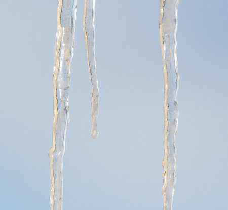 A long icicle hanging from a roof. The icicle is clear and has a slight sheenの写真素材