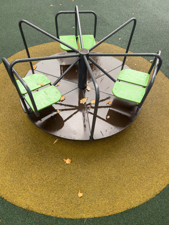 A round playground with a green and black seat. The green seat is located on the left side of the...