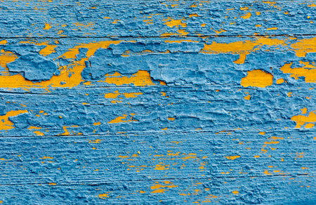 A blue and yellow wall with peeling paint. The blue is more prominent than the yellow. The wall is made of woodの写真素材