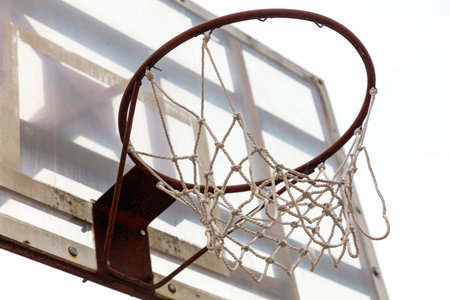 A basketball net is hanging from a metal pole. The net is white and has a few holes in itの写真素材