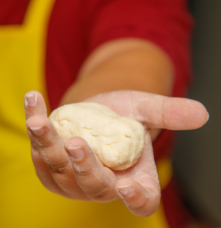 A person is holding a dough ball in their hand. The dough ball is white and has a slightly rough...