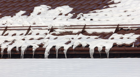 A roof covered in snow and icicles. The roof is brownの写真素材