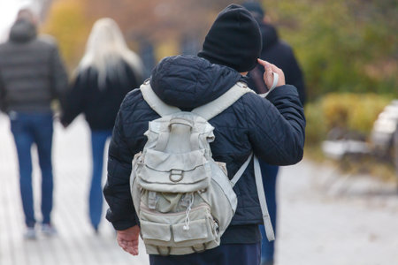 A man wearing a backpack and a black hat is talking on a cell phone. He is walking down a sidewalk