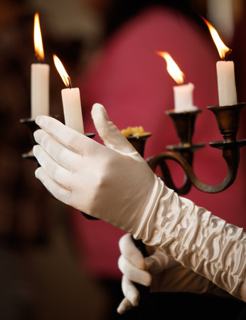 A person is holding a candle holder with four candles. The candles are lit and the person is wearing glovesの写真素材