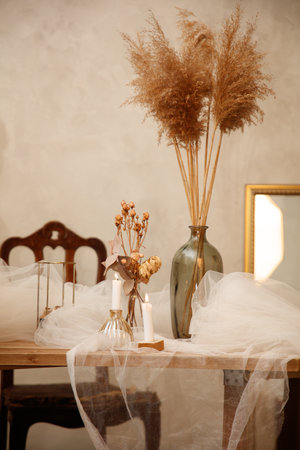 A table with a vase of flowers and candles on it. A chair is next to the tableの写真素材