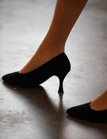 A woman wearing black high heels. The heels are pointed and the woman is standing on a concrete floorの写真素材