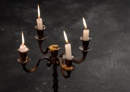 A candle holder with four candles in it. The candles are lit and one of them is meltedの写真素材