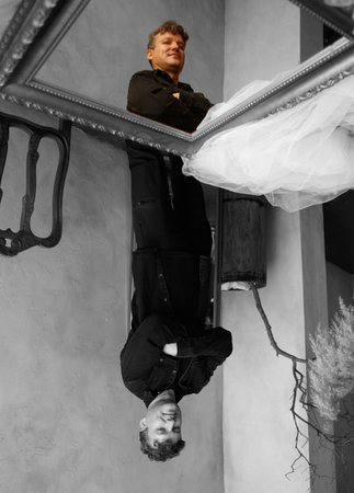 A man stands in front of a mirror. The man is wearing a black shirt and black trousers.の写真素材