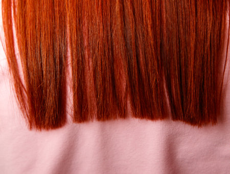 A woman with red hair has her hair cut in a straight line. The hair is long and red, and it is visible from the neck down to the waist. The woman is wearing a pink shirtの写真素材