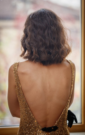 A woman in a gold dress with a black glove on her right hand. She is looking out the windowの写真素材