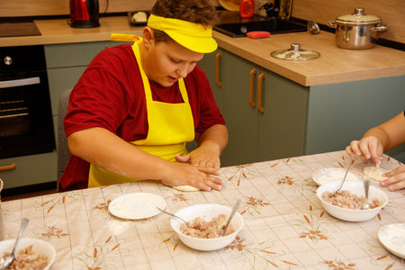 A boy in a red shirt and yellow apron is making food. There are several bowls on the table, and a spoon is in one of themの写真素材