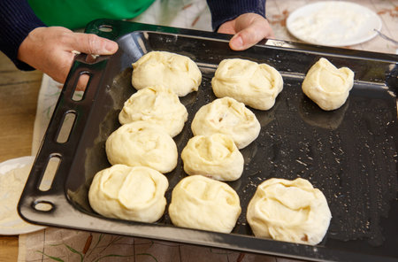 A person is holding a tray with a dozen dough pieces. The dough pieces are all the same size and are...