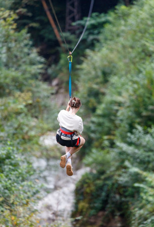 A woman is hanging from a zip line. She is wearing a white shirt and black shortsの写真素材