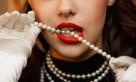 A woman is wearing a pearl necklace and white gloves. She is biting into a pearl necklace. The necklace is made of pearls and is longの写真素材