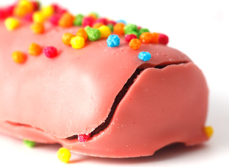 A pink bar of candy with colorful sprinkles on top. The sprinkles are in various colors including...