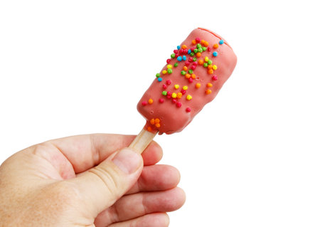 A hand holding a pink ice cream stick with rainbow sprinkles. The stick is pink and has sprinkles on...