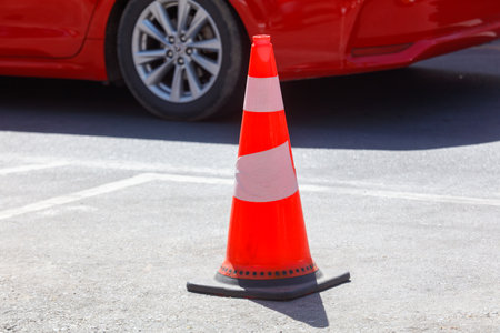 A red cone is on the ground in front of a car. The cone is orange and has a white stripeの写真素材