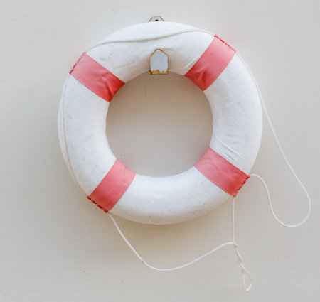 A white and red life preserver with a red band. The band is tied to a ropeの写真素材