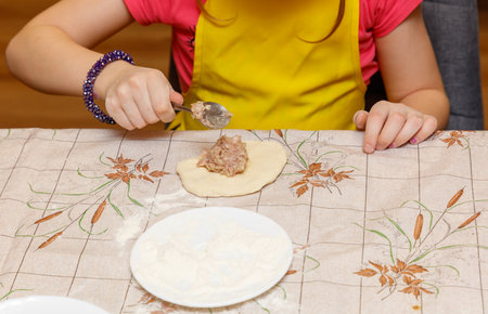 A girl is making a sandwich on a table. She is wearing a yellow apron. The table is covered with a floral patterned clothの写真素材