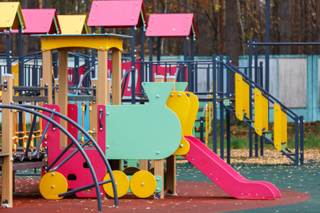 A colorful train is on a playground. The train is yellow and green. There is a slide next to the trainの写真素材