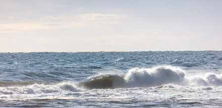 The ocean is calm and the waves are small. The sky is cloudy and the sun is low in the skyの写真素材
