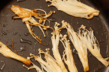 Enoki mushrooms are fried in a pan.