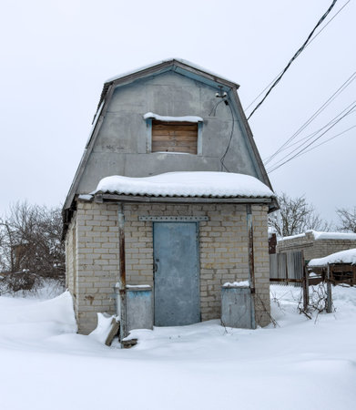 A small building with a blue door and a window. The door is open. The building is covered in snowの写真素材