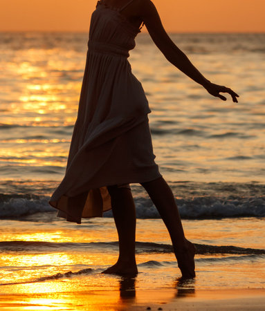 A woman is standing in the ocean with her feet in the water. She is wearing a dressの写真素材