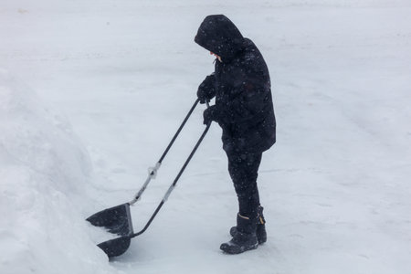 A boy clears snow with a big shovel in winter.
