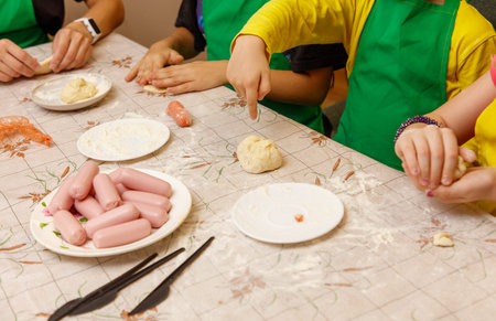 A group of children are making food on a table. There are plates of food and a plate of dough