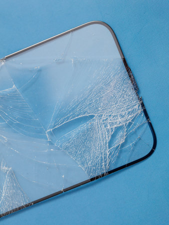 Broken smartphone screen with cracked glass on blue surfaceの写真素材
