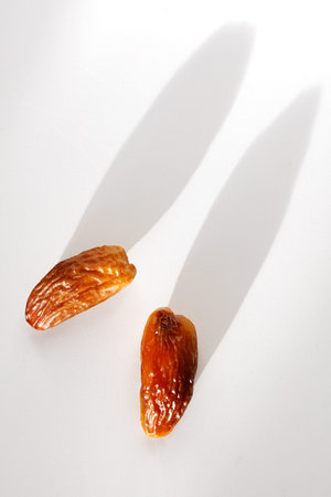 Two dried dates on white surface. Bright shadows cast behind them. Food photography with simple...