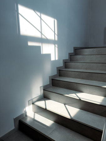 Sunlight casts sharp shadows across modern concrete stairs. White walls contrast with gray steps....