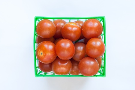Fresh tomatoes in green plastic basket on white backgroundの写真素材