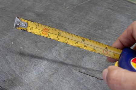 Woman's hand holding tape measure on wood backgroundの写真素材