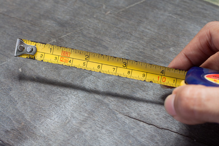 Woman's hands holding tape measure on wood backgroundの写真素材