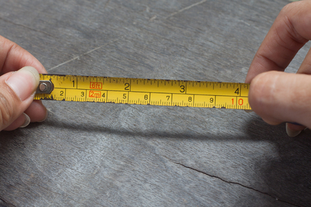 Woman's hands holding tape measure on wood backgroundの写真素材