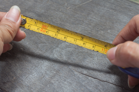 Woman's hands holding tape measure on wood backgroundの写真素材