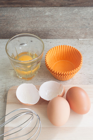 ingredients and tools to make a cake, eggs, bakery cups on wood tableの写真素材