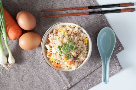 Bowl of fried rice, carrot and egg on pink fabric, spoon, chopsticks and ingredients for backgroundの写真素材