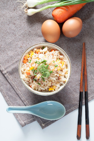 Bowl of fried rice, carrot and egg on pink fabric, spoon, chopsticks and ingredients for backgroundの写真素材