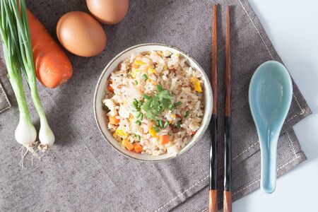 Bowl of fried rice, carrot and egg on pink fabric, spoon, chopsticks and ingredients for backgroundの写真素材